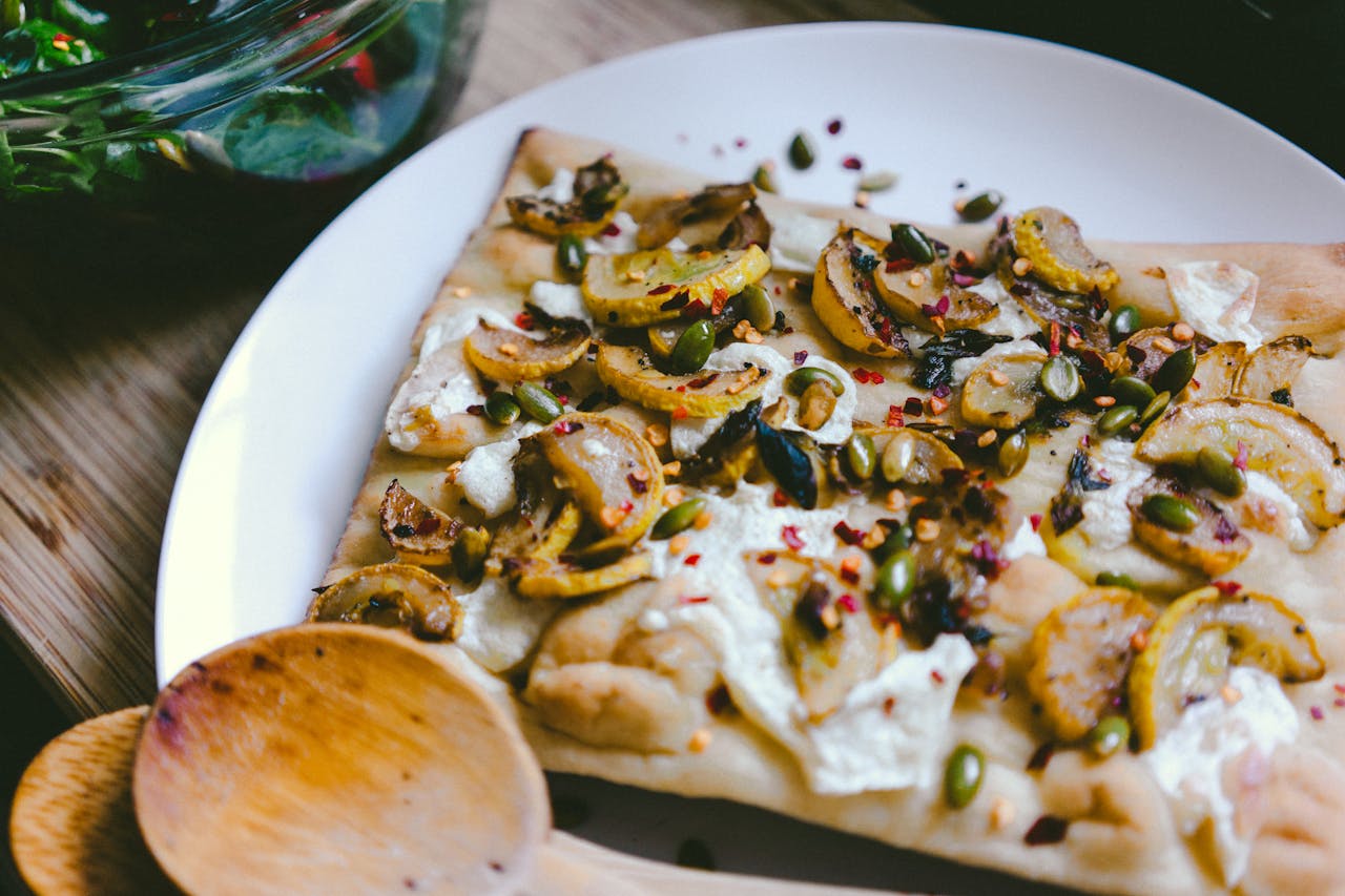 Delicious flatbread topped with squash, seeds, and cheese on a ceramic plate.