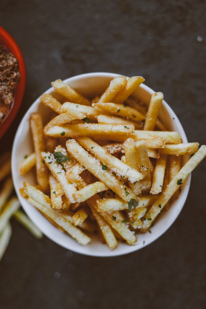A bowl of crispy, delicious french fries garnished with herbs on a dark background.